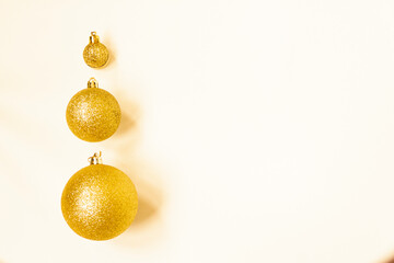 Three golden Christmas balls of different sizes are displayed in a row as a border on a white background. Copy space.