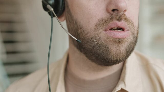 Extreme close-up of bearded male person cropped below eyes part of face on blurred background indoors. Man wearing headset talking