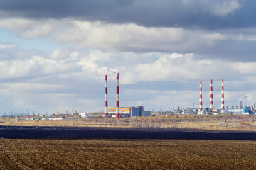 Fototapeta na wymiar Autumn landscape with a plowed field, CHP and gas processing plant on the horizon. The picture was taken in Russia, in Orenburg