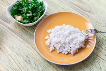 White boiled rice and greens salad on a wooden background. Healthy food concept.