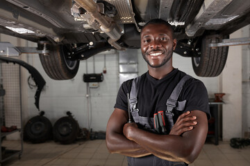 portrait of positive afro american auto mechanic in uniform posing after work, he is keen on...