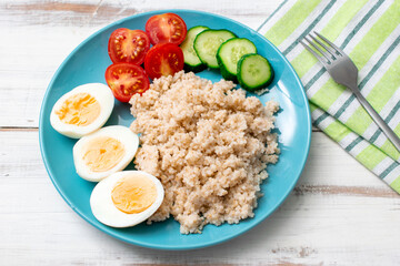 Healthy food, diet. Barley porridge, chicken eggs and vegetables on a wooden background.
