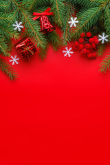 Christmas greeting card with fir tree branches, gift box, bell, white snowflakes and berries on red background. Vertical orientation, copy space for text 