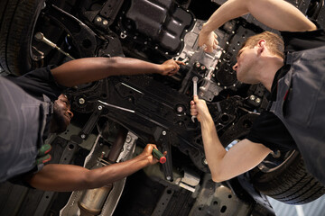 two mixed race auto mechanic males have successful work together, they are repairing car bottom