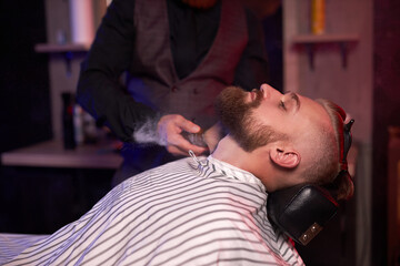 Fototapeta premium modern barber male begins to cut hair of client, making stylish beard, hair cut in salon