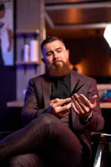 close-up photo of scissors in hands of professional male barber, handsome guy in suit examining, checking scissors for future cutting hair of clients