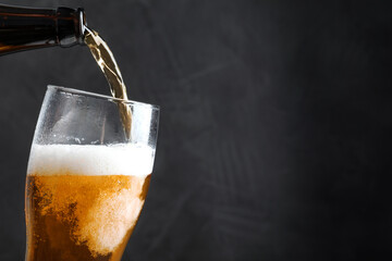Pouring cold tasty beer from bottle into glass on black background, closeup. Space for text