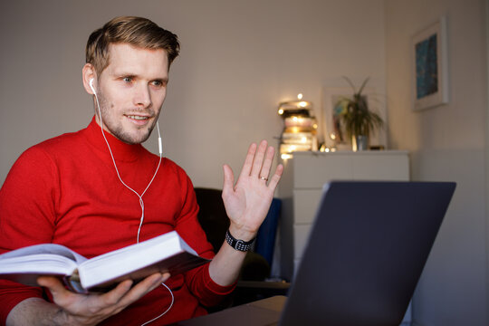 Handsome Young Man In Casual Red Clothes Reading A Book In A Video Teacher Call. Book Club Online  Social Distancing. Online Education In Video Conferencing. Virtual Bible Study. Internet Book Circle