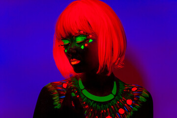 Close up portrait of a girl with artistic neon colorful makeup and orange wig, isolated violet blue background.