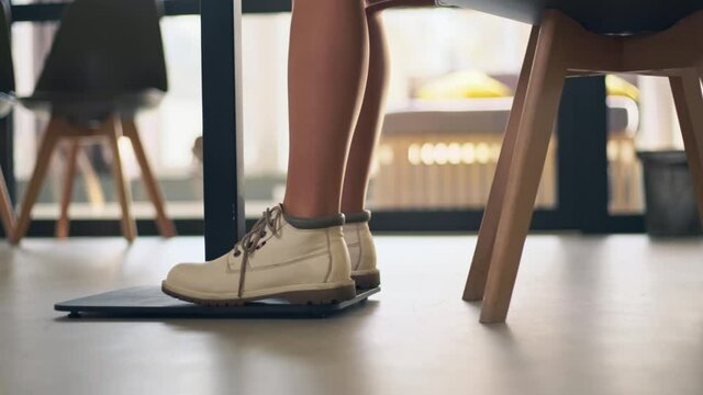 Working at office comfortably. Young woman in white boots stepping rhythm at workplace under table, close up
