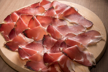 Speck, typical smoked ham from South Tyrol, Alto Adige in Italy - slices on wooden cutting board in...
