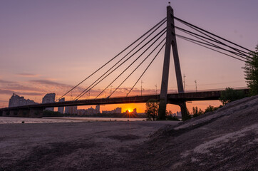 Large cable-stayed bridge over the river. Sunset behind the bridge.