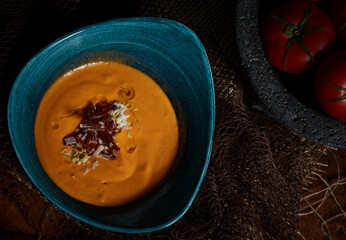 Typical Spanish salmorejo cream with ham and egg on wooden table. Top view.