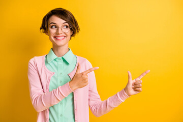 Photo of lady direct fingers look empty space toothy smile wear glasses teal shirt pink cardigan isolated yellow color background