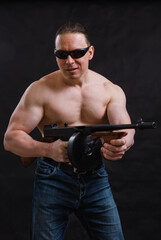 Fototapeta na wymiar Mature man in sunglasses and naked torso with tommy gun