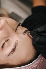 Close-up girl's face with closed eyes. The hand of a master beautician draws a sketch of an eyebrow...