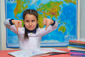 Portrait of a smart cute girl showing thumbs down on the background of the world map.