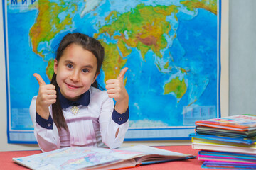 Portrait of a smart cute girl showing thumbs up on the background of the world map.