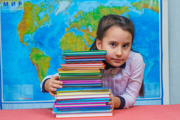 Portrait of a smart cute girl hugging a lot of books on the background of the world map.