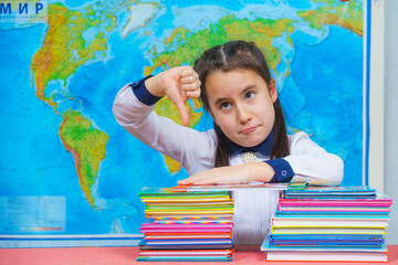 Portrait of a smart cute girl hugging a lot of books on the background of the world map. Thumbs down
