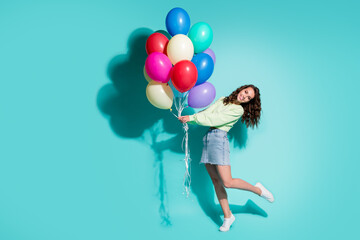 Photo of cute young girl hold many balloons dance wear sneakers green pullover mini jeans skirt isolated blue color background
