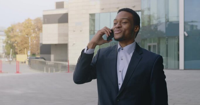 Outdoor portrait of handsome black businessman having joyful phone talk, conversating with partners and smiling