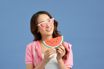 Happy young Asian girl holding watermelon slice over blue background.
