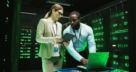 African American man with laptop computer and Caucasian woman with tablet device talking and...