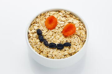 A cup of dry oatmeal with dried fruits smile on a white background.