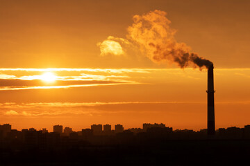 Sunrise over the silhouette of houses on the outskirts of the metropolis landscape with a Smoking pipe in Russia