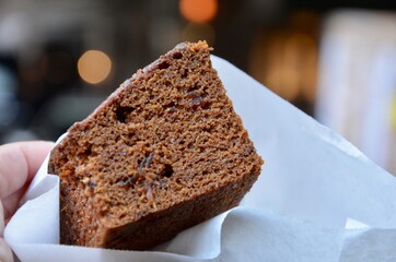 One piece of a traditional British spiced gingerbread cake in a white paper bag during christmas time, bokeh background