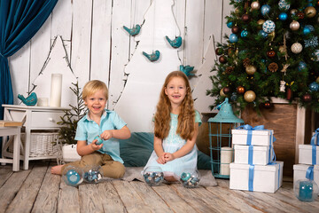 redhead girl and blonde boy are sitting on the wooden floor christmas tree