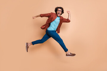Fototapeta na wymiar Photo portrait full body view of laughing running guy jumping up isolated on pastel beige colored background