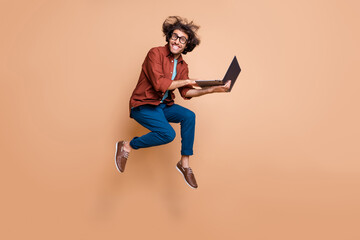 Full length photo portrait of excited guy jumping up with laptop in hands isolated on pastel beige...