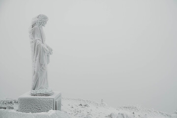 The statue of Jesus is covered with snow and ice on top of the mountain. Copy, empty space for text