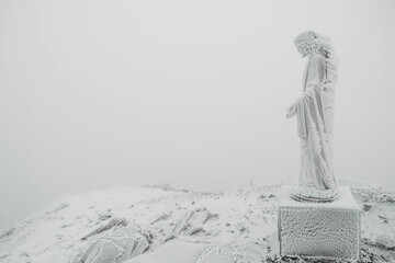 The statue of Jesus is covered with snow and ice on top of the mountain. Copy, empty space for text