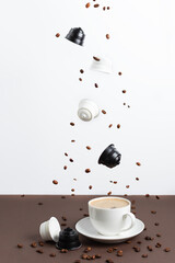 Espresso coffee capsules and roasted coffee beans levitating above coffee cup.