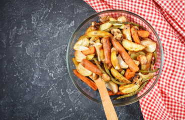 Baked vegetables on black stone background. Potatoes, carrot, mushrooms and onions.