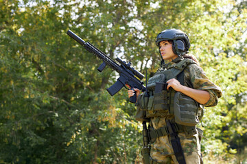 strong brave female army soldier with rifle machine gun standing in the forest, she is ready to shoot at enemy, firearm outdoor shooting range