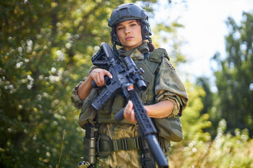 young caucasian military woman holds a gun in her hand in nature, she is going to hunt, hunting in forest is a hobby. game with weapons
