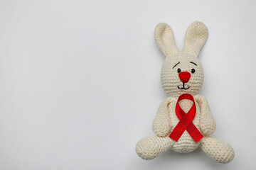 Cute knitted toy bunny with red ribbon on light grey background, top view and space for text. AIDS disease awareness