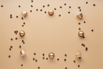 Caffeine, hot drinks and objects concept - close up of golden capsules or pods for coffee mashine with some roasted grains on beige background. Top view with space for text. Flat lay..