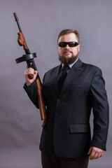 Mature man in sunglasses dressed in suit with tommy gun