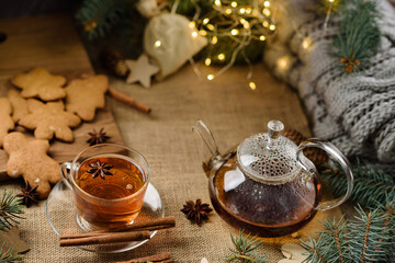 A glass cup of tea and a transparent teapot shot with selective focus against a backdrop of festive decor.