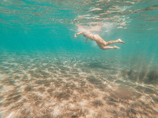 Underwater view in blue sea ocean water of active woman swimming and enjoying the summer holiday vacation at the beach