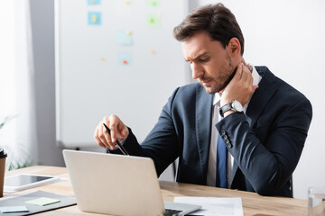 Businessman with painful neck sitting at workplace on blurred background