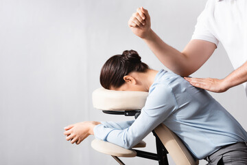 Side view of masseur massaging woman back with elbow, sitting on massage chair on white background - obrazy, fototapety, plakaty