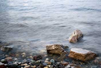 The stones lie near the shore in the waves of the muddy surf