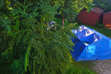 Two metal garages, a white car behind the trees and a plastic te