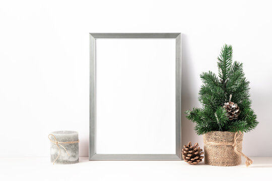 Photo or poster mockup with a silver frame, small decorative christmas tree  and candle